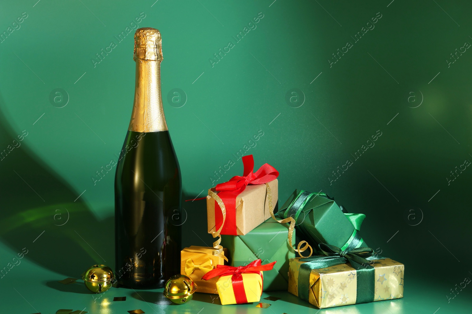 Photo of Bottle with sparkling wine, confetti and gift boxes on green background