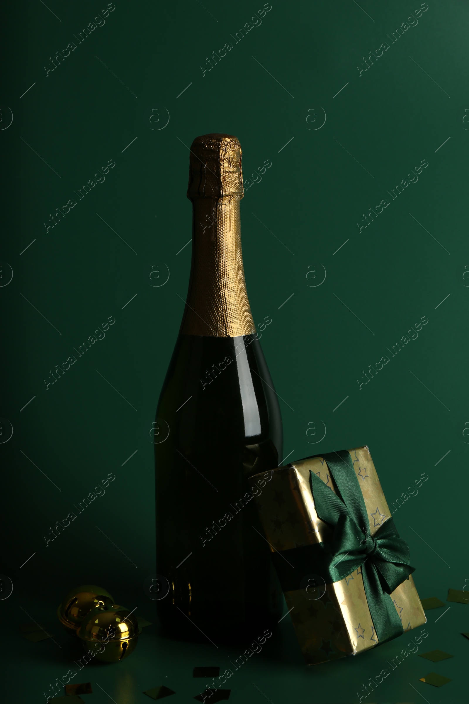 Photo of Bottle with sparkling wine, confetti and gift box on green background