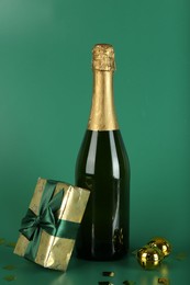 Photo of Bottle with sparkling wine, confetti and gift box on green background