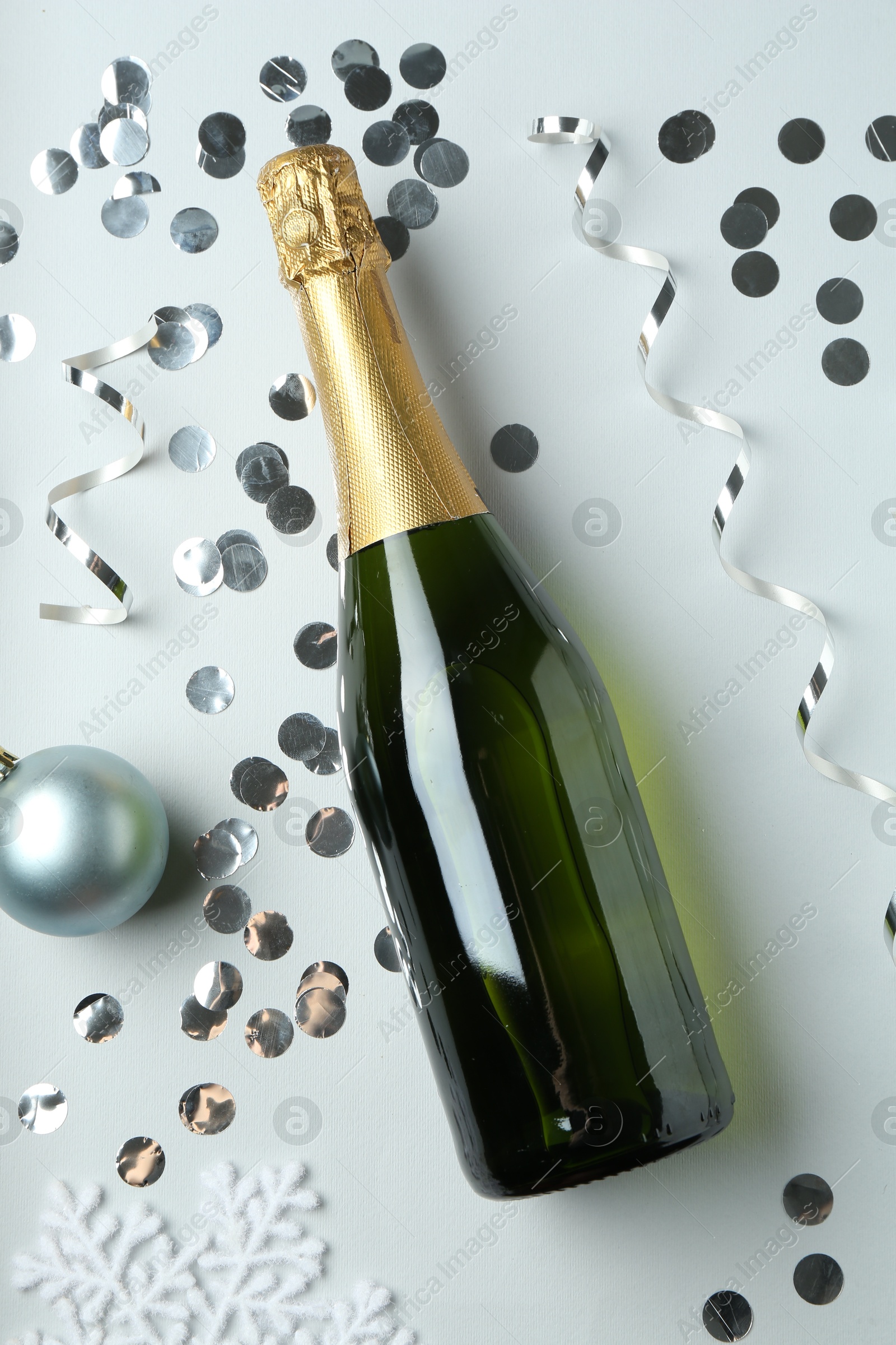 Photo of Flat lay composition with bottle of sparkling wine, shiny confetti and other Christmas decor on light grey background