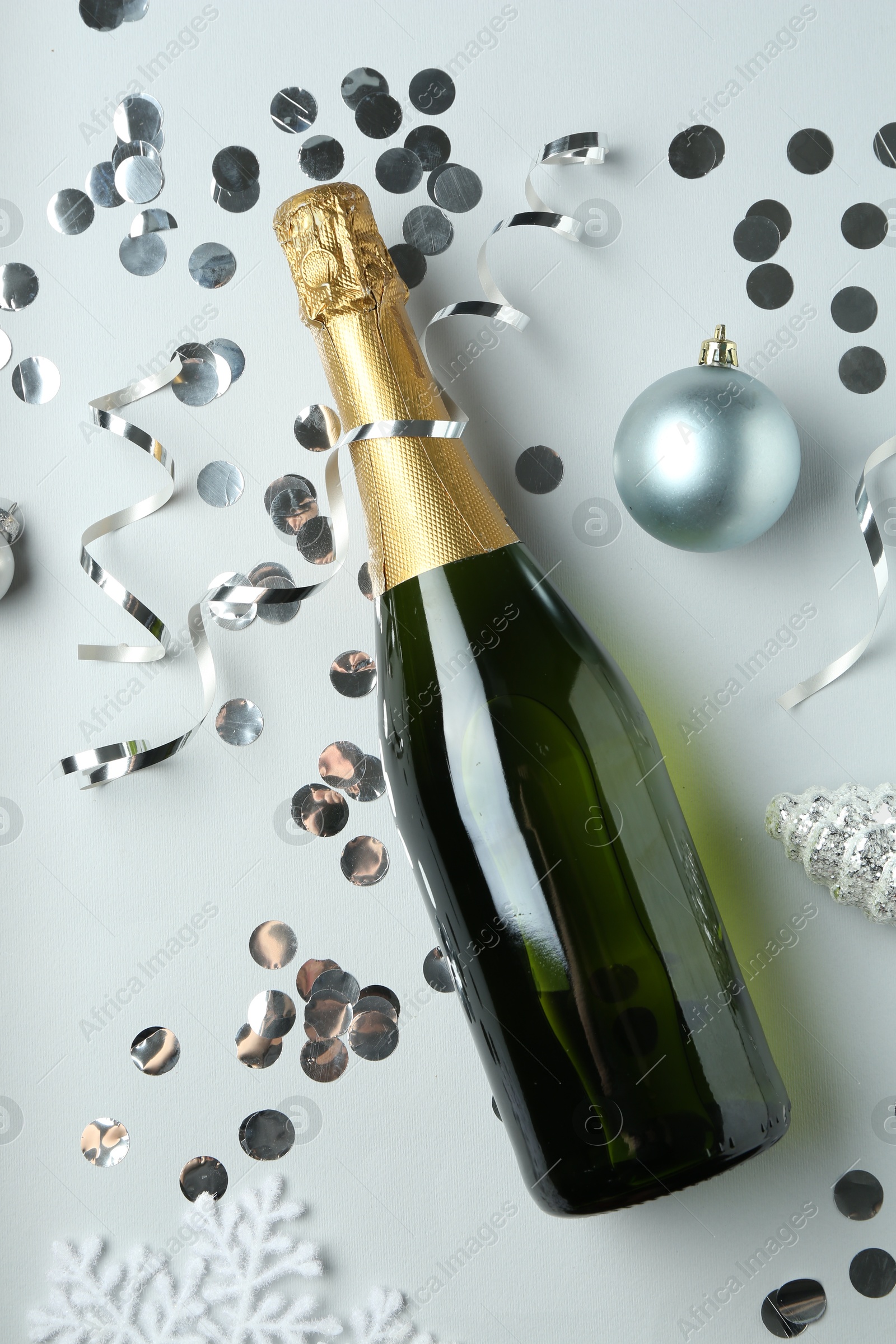 Photo of Flat lay composition with bottle of sparkling wine, shiny confetti and other Christmas decor on light grey background