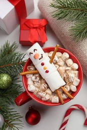 Photo of Funny snowman made with marshmallows in cup of hot drink and Christmas decor on white table, flat lay