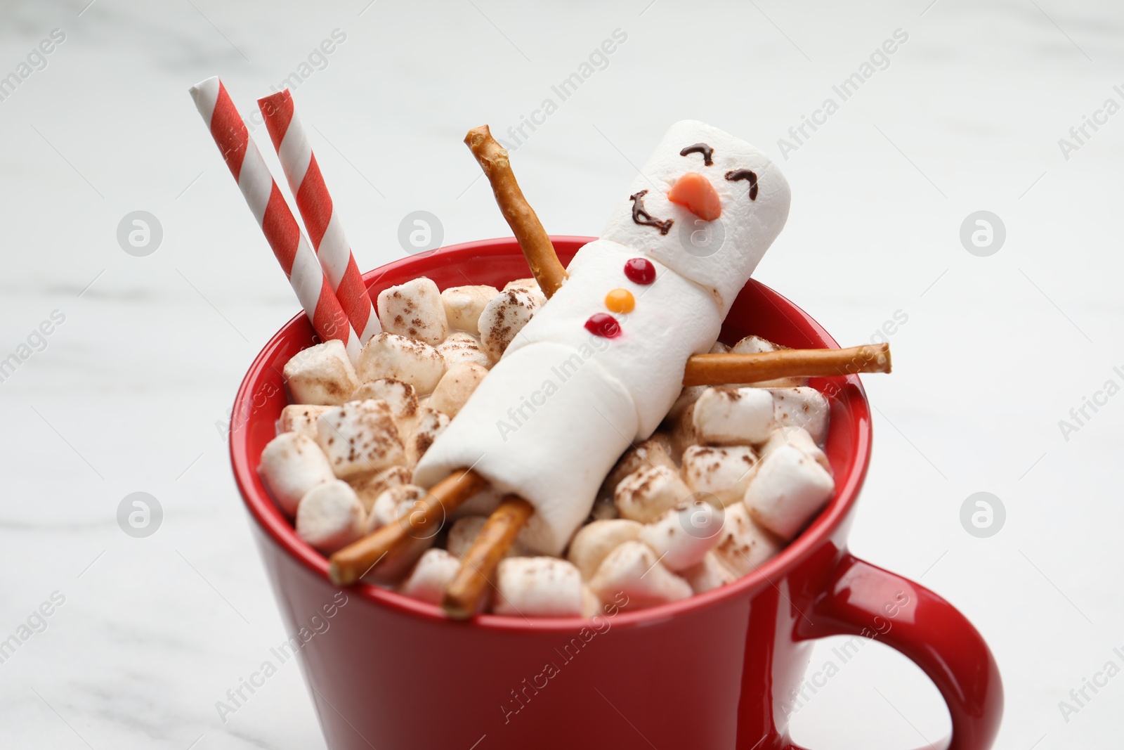 Photo of Funny snowman made with marshmallows in cup of hot drink on white table, closeup