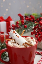 Funny snowman made with marshmallows in cup of hot drink and Christmas decor on white table, closeup