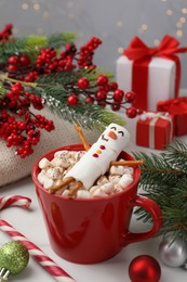 Funny snowman made with marshmallows in cup of hot drink and Christmas decor on white table