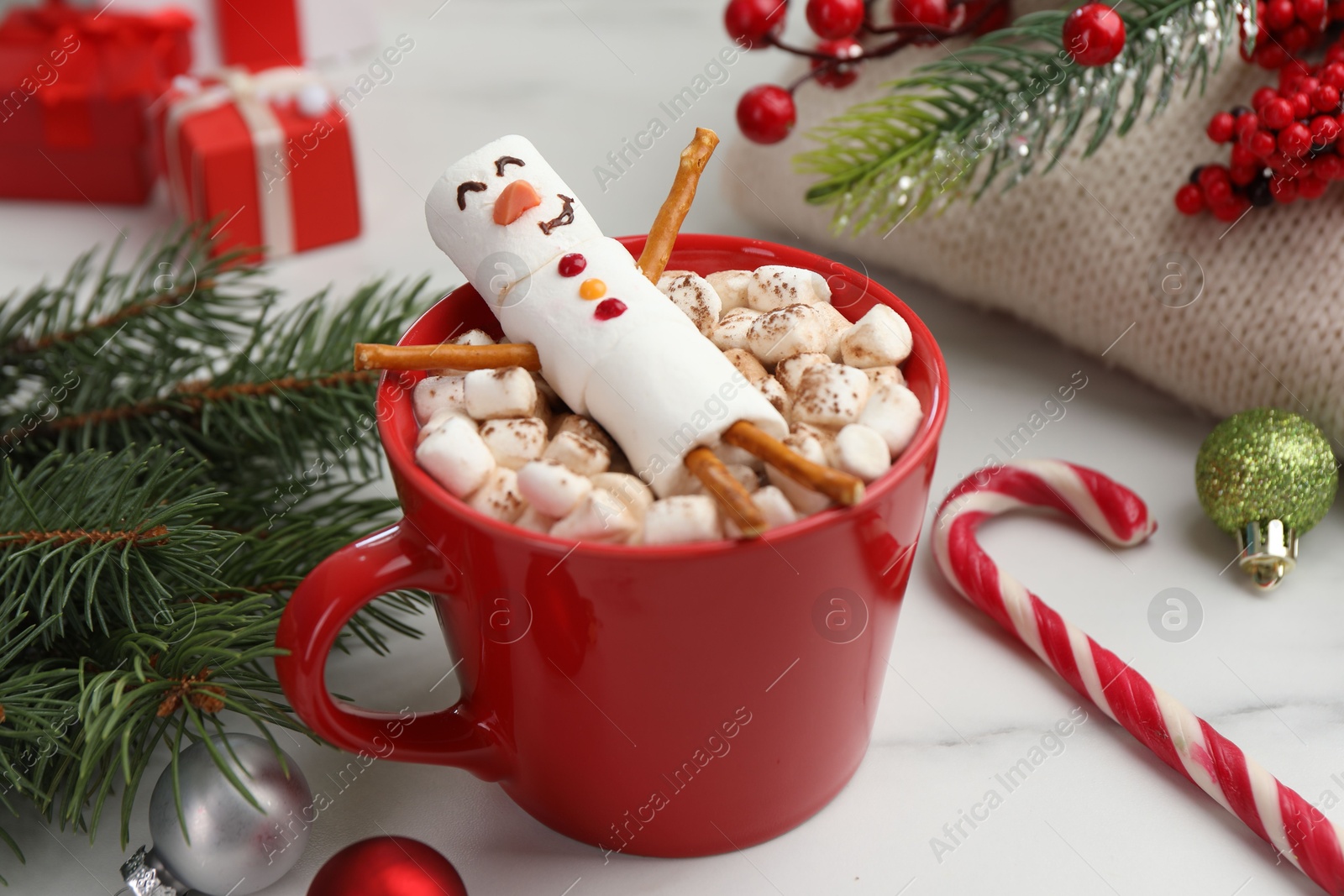 Photo of Funny snowman made with marshmallows in cup of hot drink and Christmas decor on white table, closeup