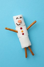 Photo of Funny snowman made of marshmallows on light blue background, top view