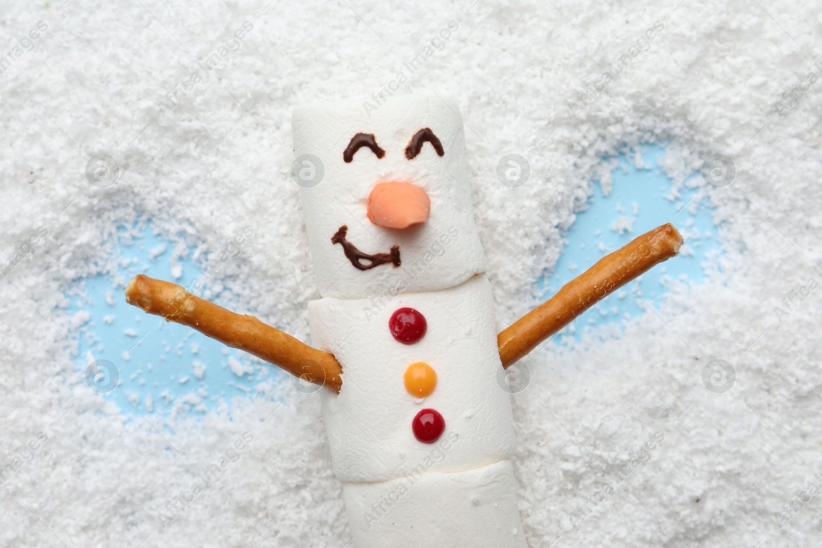 Photo of Marshmallow snowman making angel on artificial snow, top view