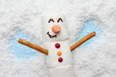 Marshmallow snowman making angel on artificial snow, top view