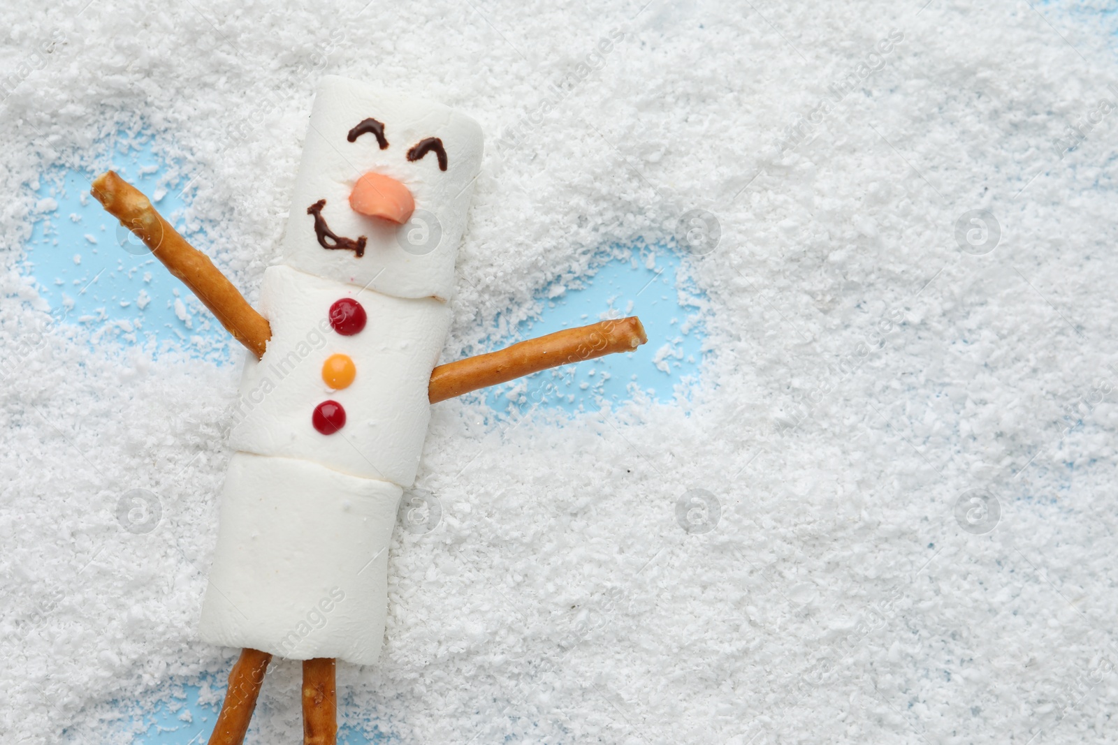 Photo of Marshmallow snowman making angel on artificial snow, top view. Space for text