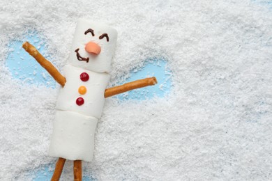 Photo of Marshmallow snowman making angel on artificial snow, top view. Space for text