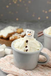 Photo of Funny snowman made with marshmallow and whipped cream in cup of hot drink served on background against Christmas lights