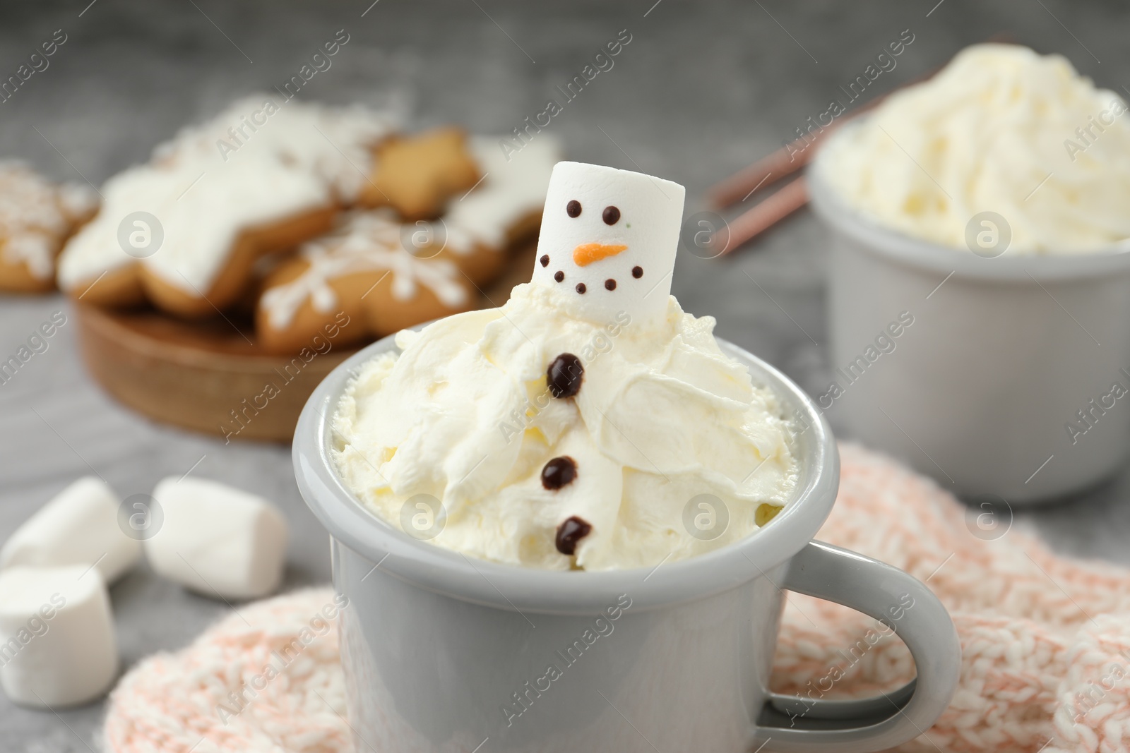 Photo of Funny snowman made with marshmallow and whipped cream in cup of hot drink served on grey background, closeup