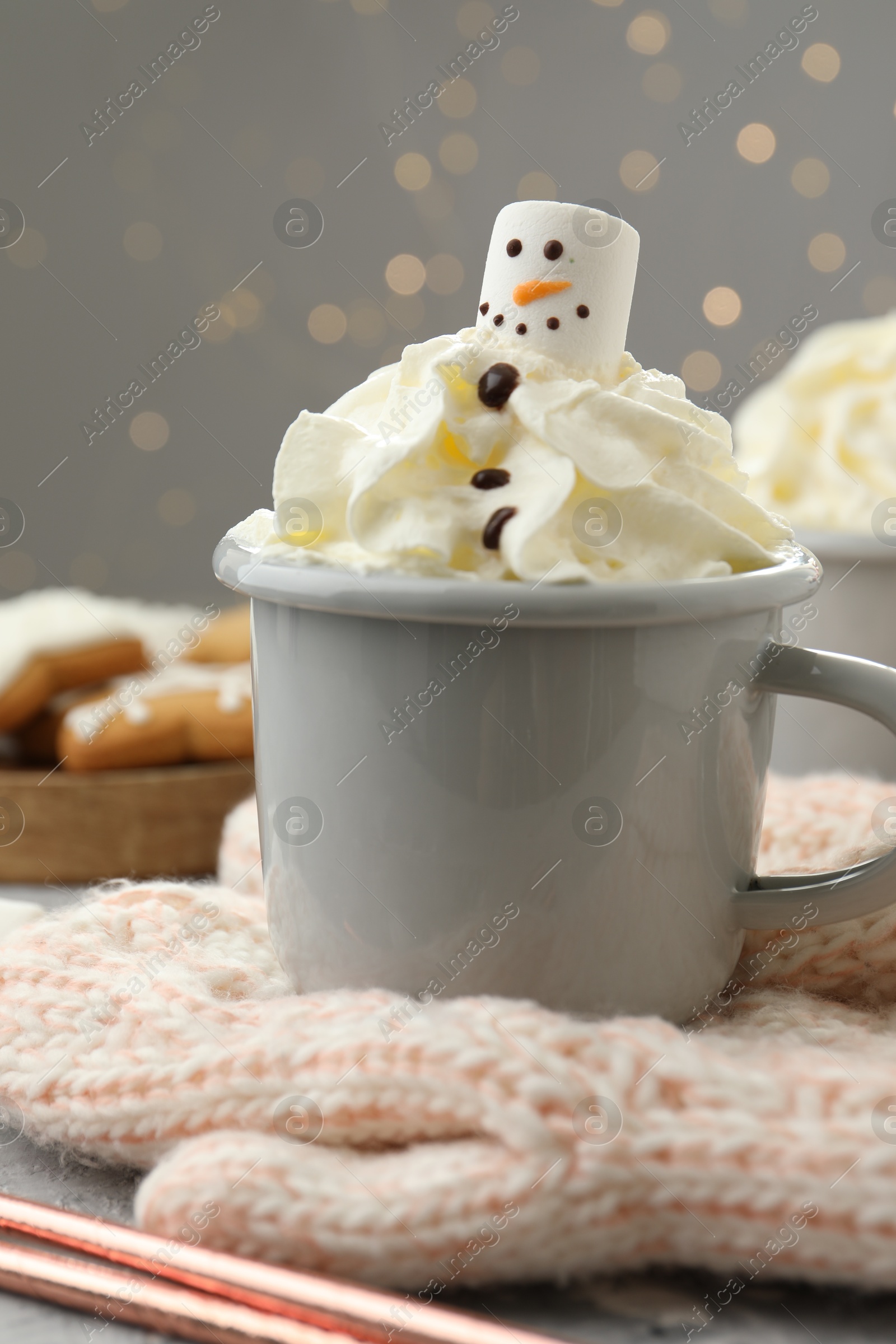 Photo of Funny snowman made with marshmallow and whipped cream in cup of hot drink served on grey background against Christmas lights, closeup