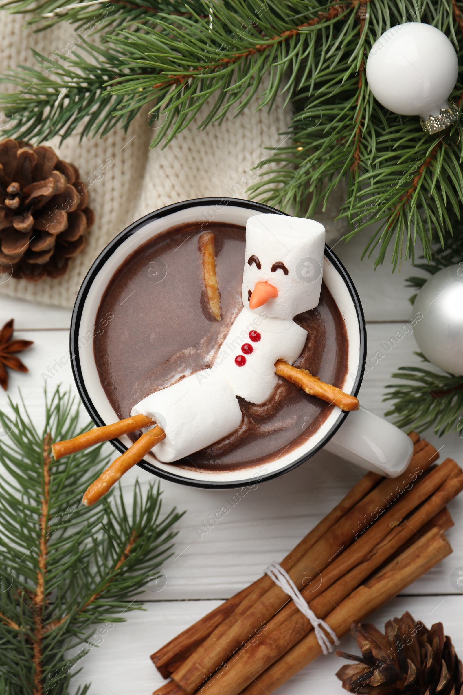 Photo of Funny snowman made with marshmallows in cup of hot chocolate and winter decor on white table, flat lay