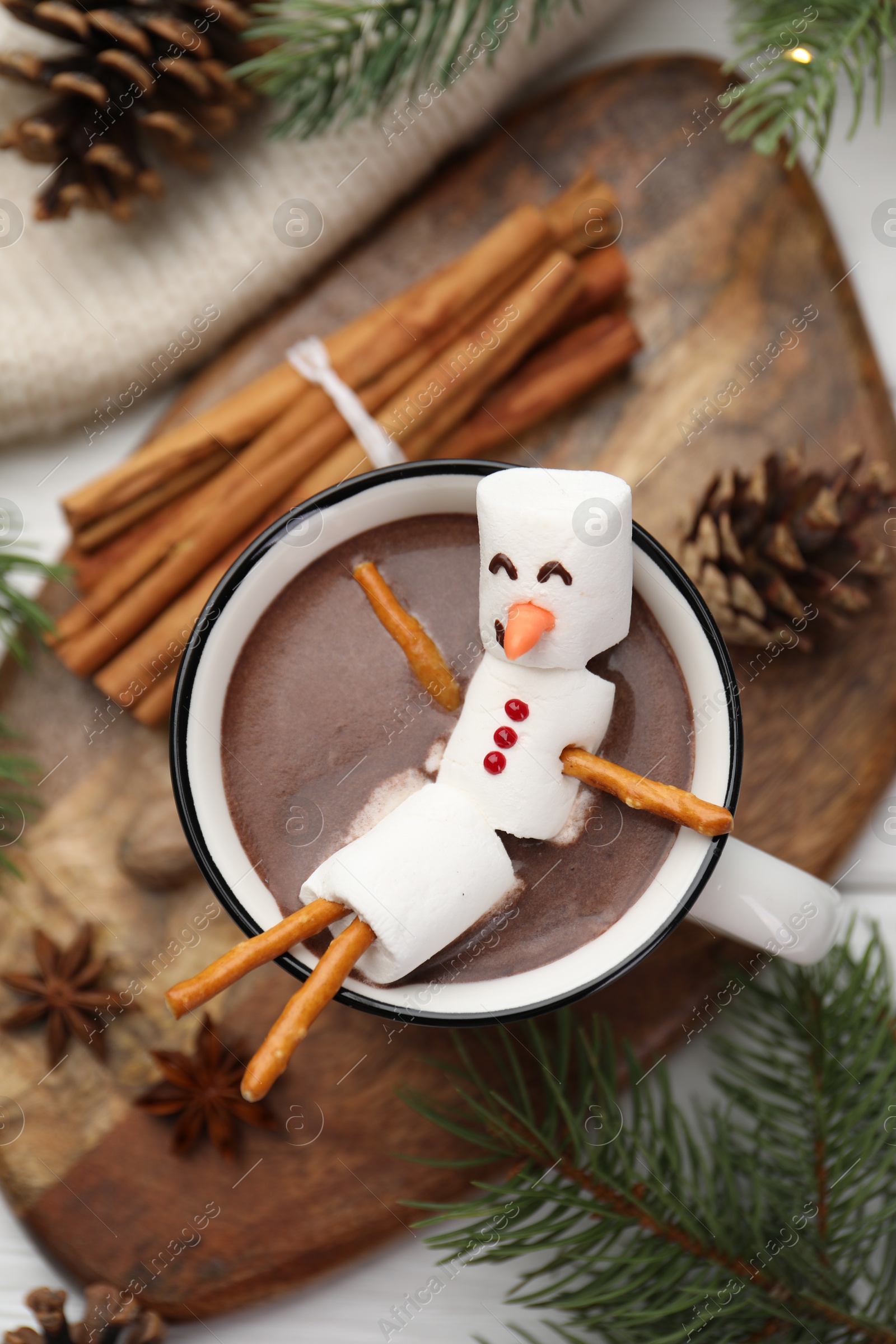 Photo of Funny snowman made with marshmallows in cup of hot chocolate and winter decor on white table, flat lay