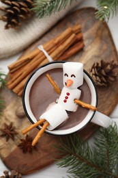 Photo of Funny snowman made with marshmallows in cup of hot chocolate and winter decor on white table, flat lay