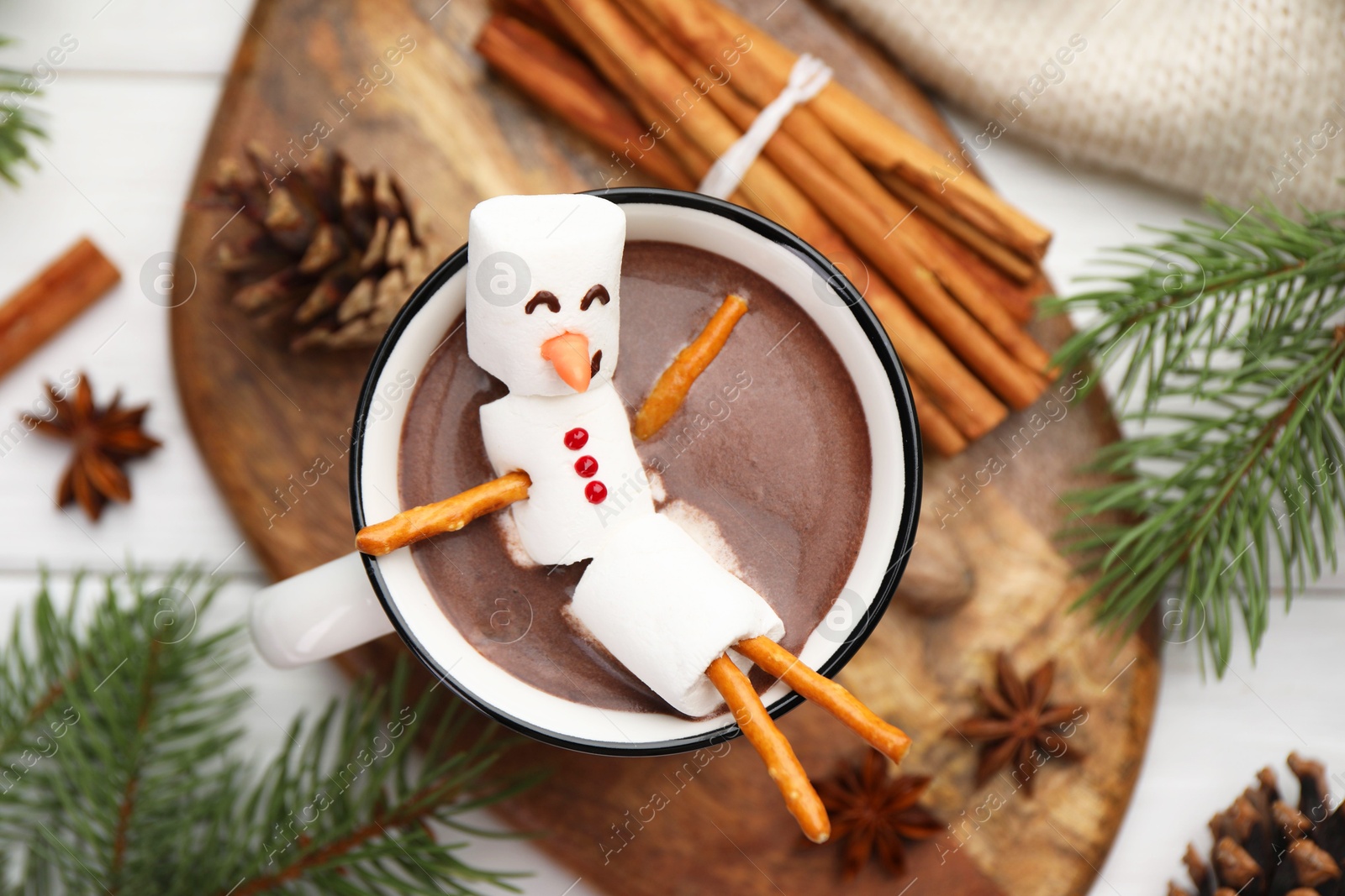 Photo of Funny snowman made with marshmallows in cup of hot chocolate and winter decor on white table, flat lay