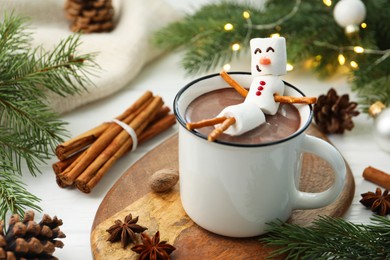 Funny snowman made with marshmallows in cup of hot chocolate and winter decor on white table