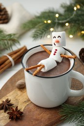 Funny snowman made with marshmallows in cup of hot chocolate and winter decor on white table