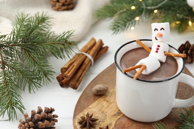 Photo of Funny snowman made with marshmallows in cup of hot chocolate and winter decor on white table