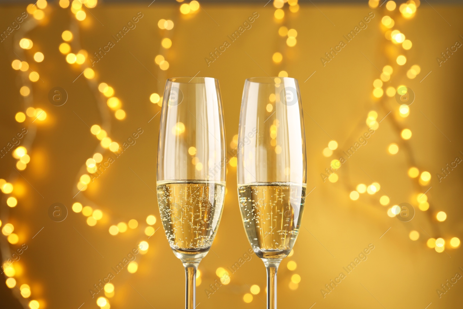 Photo of Glasses of sparkling wine against golden background with blurred lights, closeup. Christmas decor