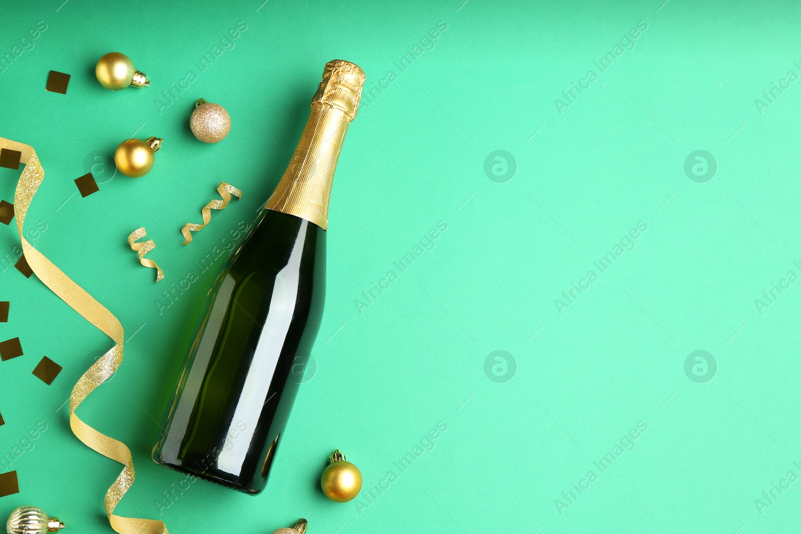 Photo of Bottle of sparkling wine, confetti and Christmas balls on green background, flat lay. Space for text