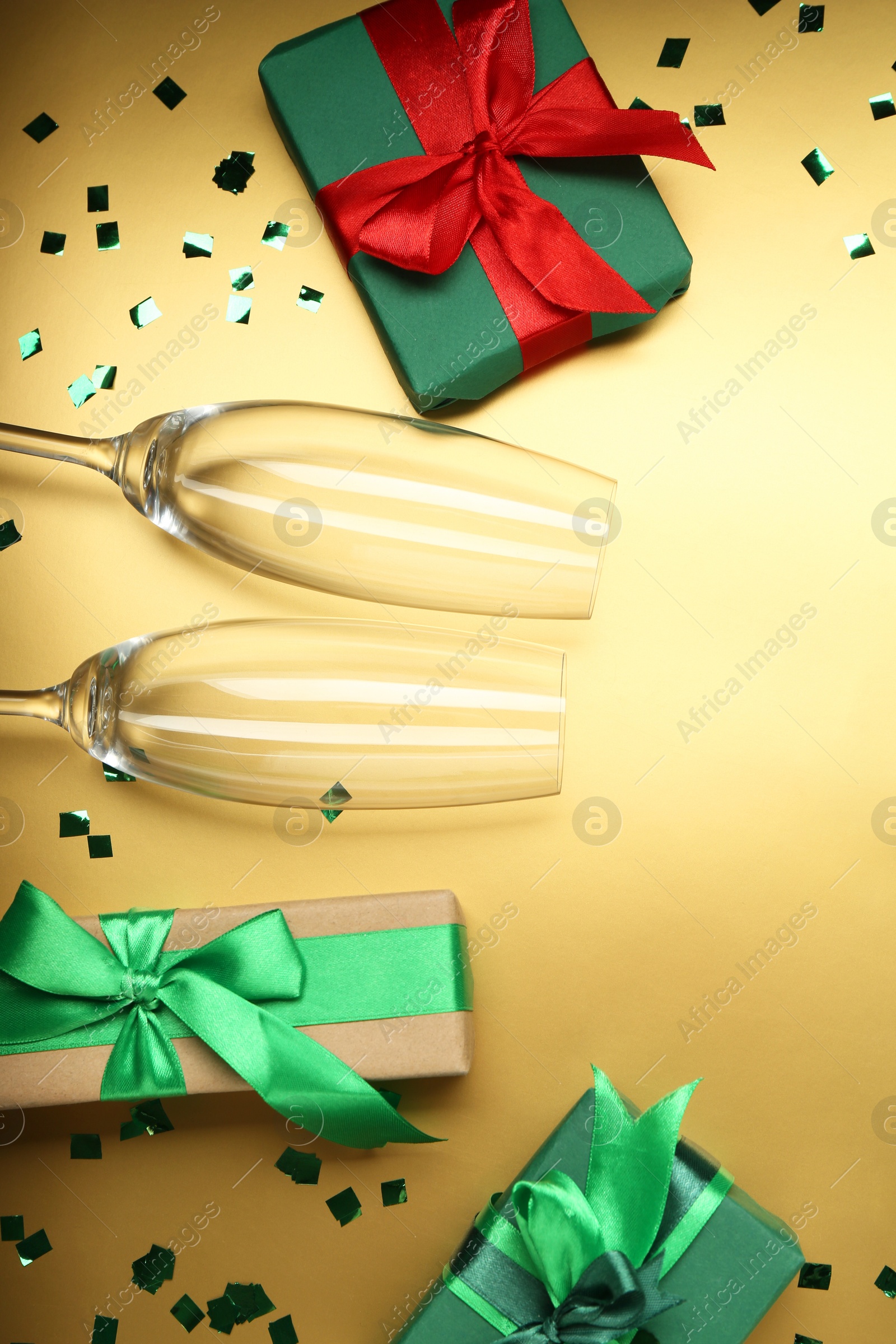 Photo of Confetti, glasses and gift boxes on golden background, flat lay. Christmas decor