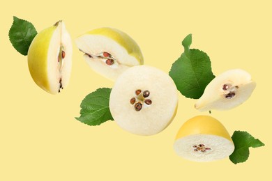 Image of Pieces of fresh quinces and green leaves flying on pale yellow background