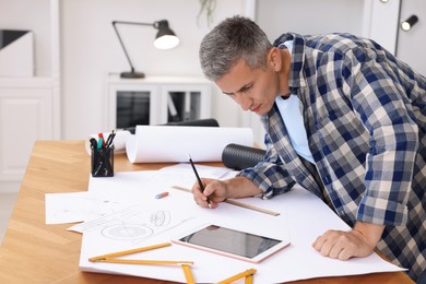 Photo of Architect making engineering drawing at wooden table in office