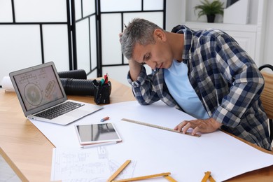 Photo of Architect making engineering drawing at wooden table in office