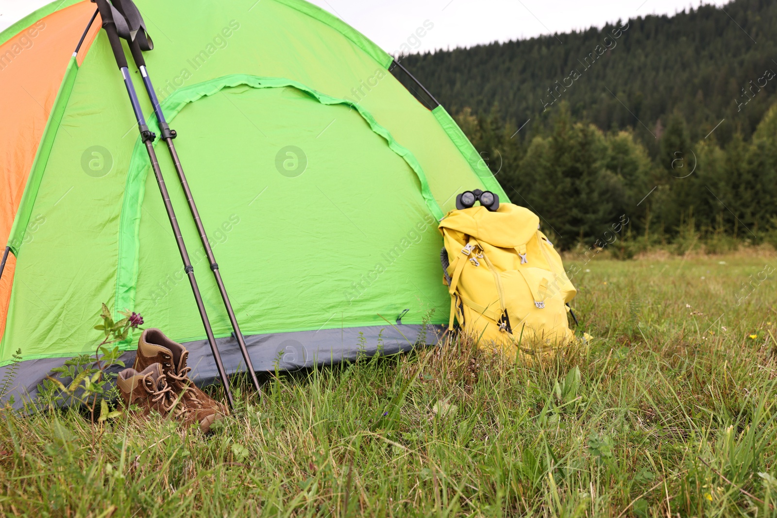 Photo of Tent, backpack and trekking poles on green grass in mountains