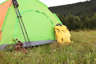 Tent, backpack and trekking poles on green grass in mountains