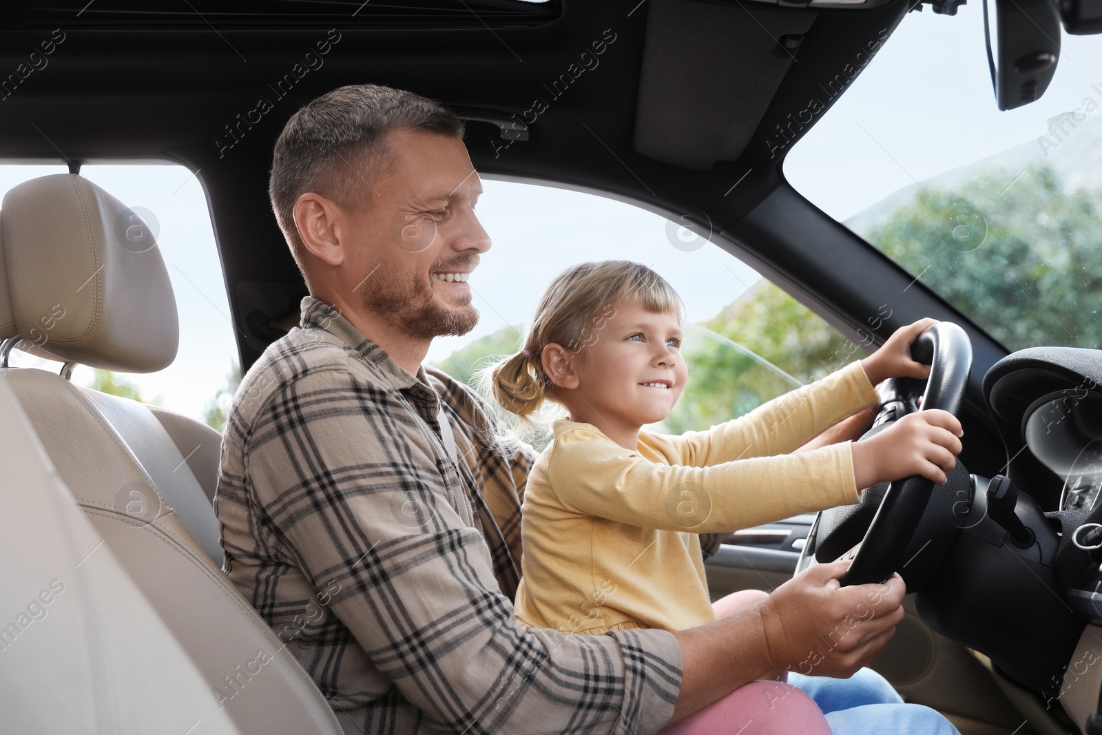 Photo of Happy man with his daughter holding steering wheel inside car