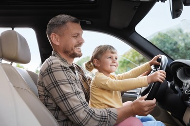 Photo of Happy man with his daughter holding steering wheel inside car