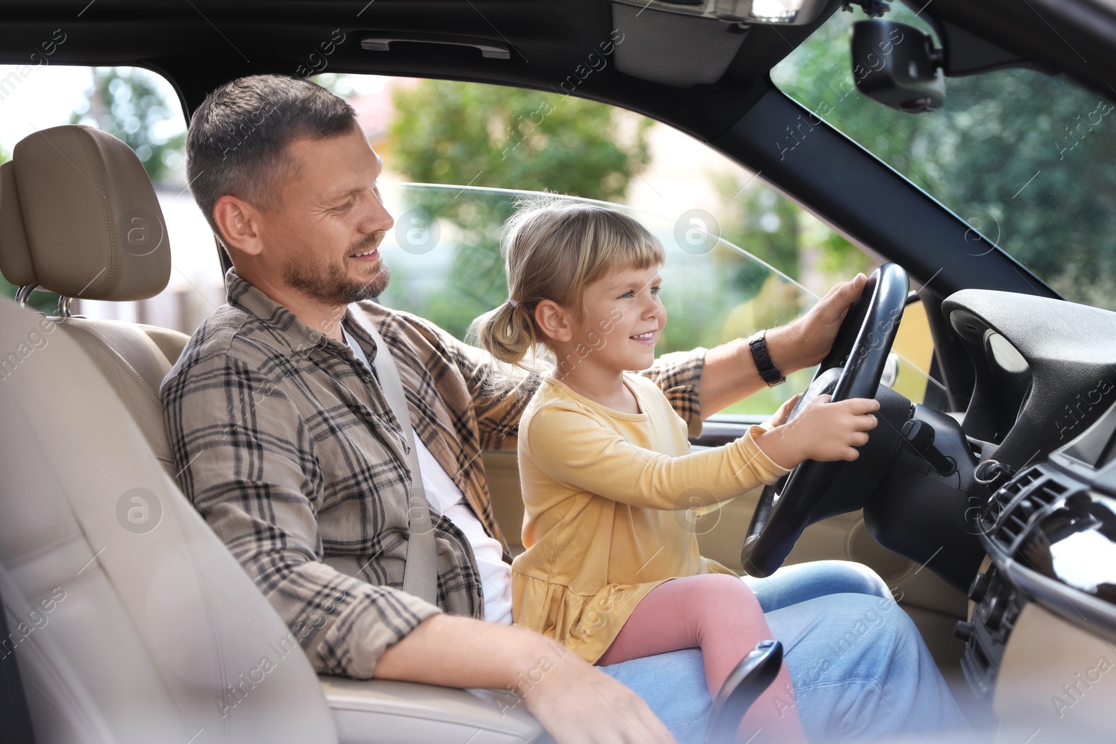 Photo of Man with his daughter holding steering wheel inside car