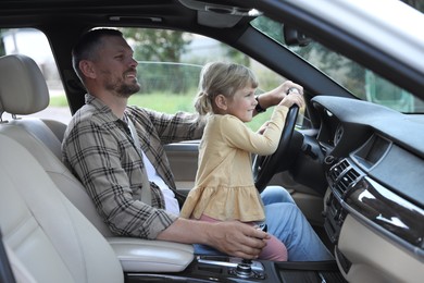 Man with his daughter holding steering wheel inside car