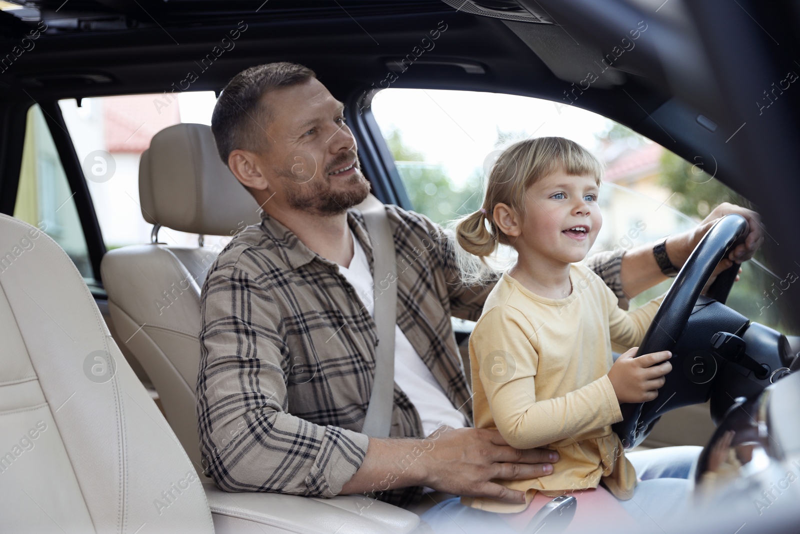 Photo of Man with his daughter holding steering wheel inside car