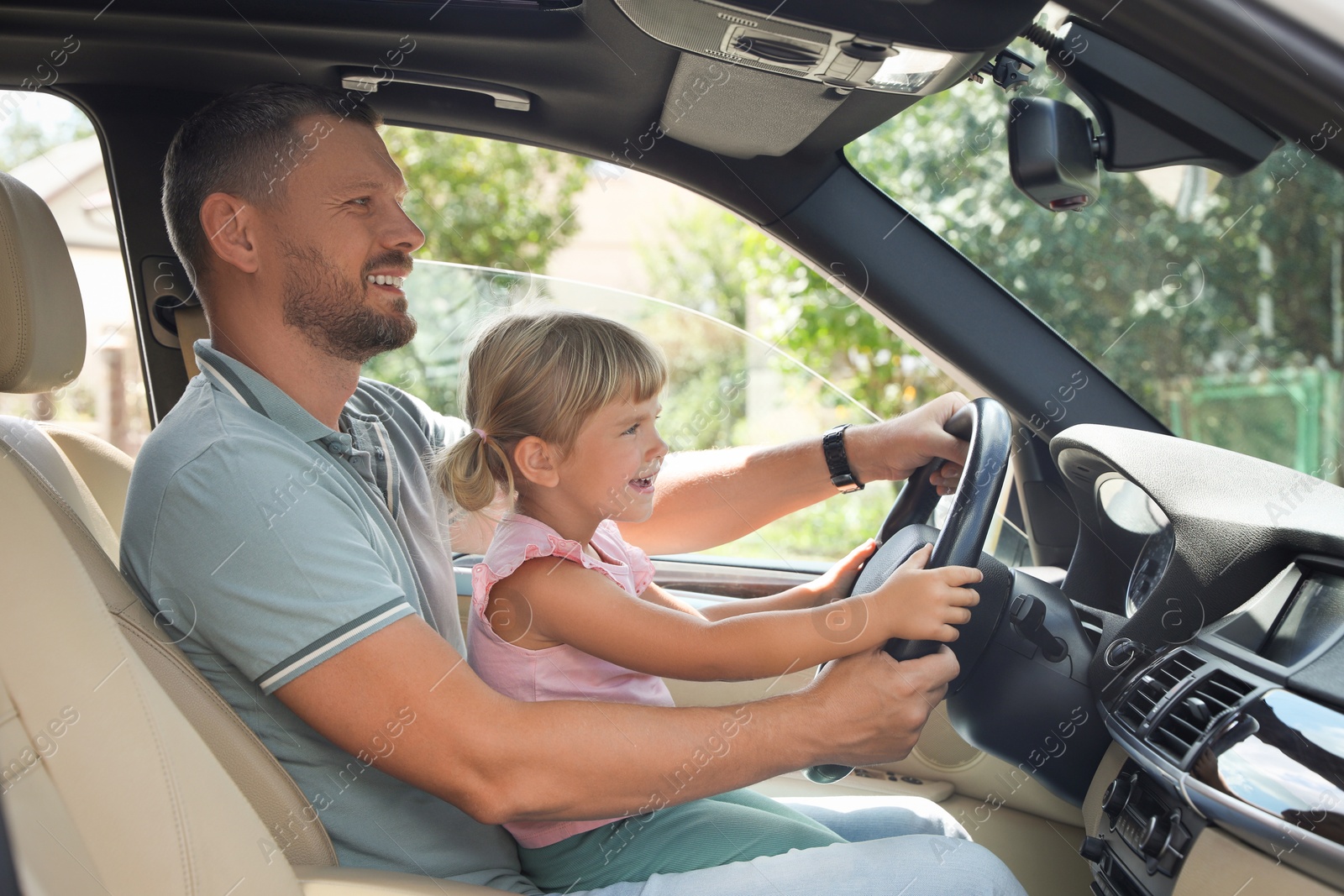 Photo of Happy man with his daughter holding steering wheel inside car