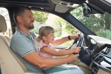 Photo of Happy man with his daughter holding steering wheel inside car