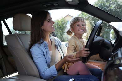 Happy woman with her daughter holding steering wheel inside car