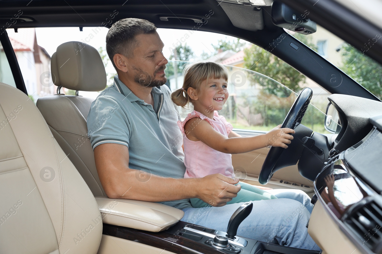 Photo of Man with his daughter holding steering wheel inside car