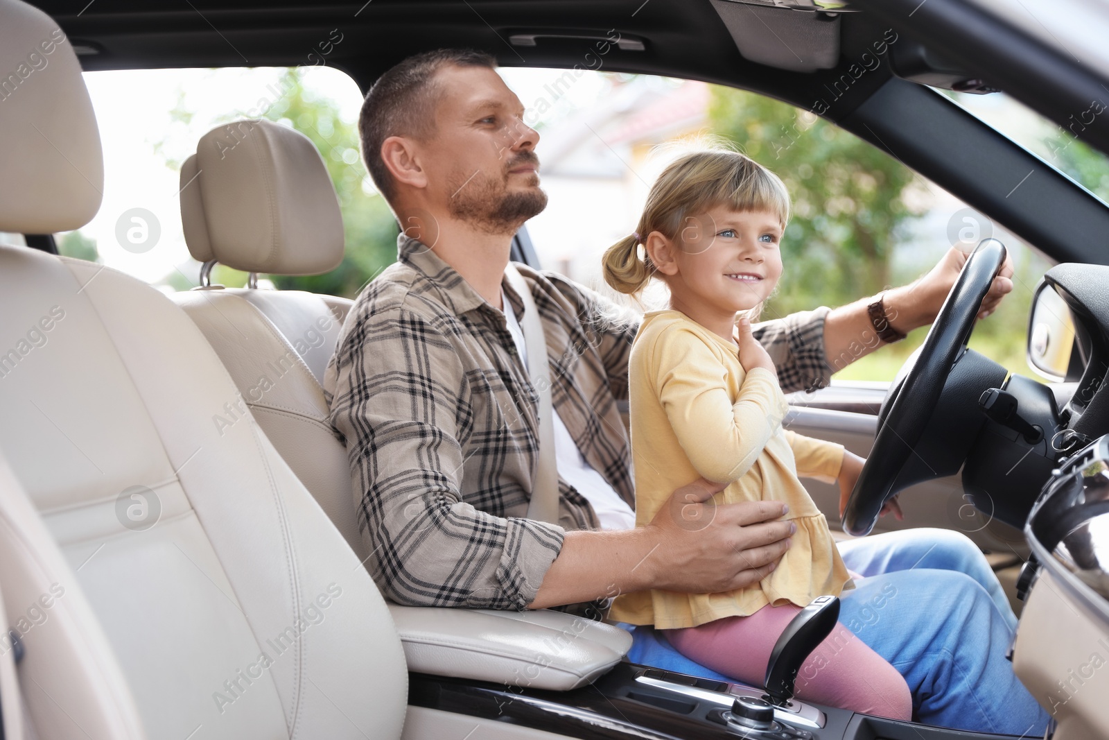 Photo of Man with his daughter holding steering wheel inside car