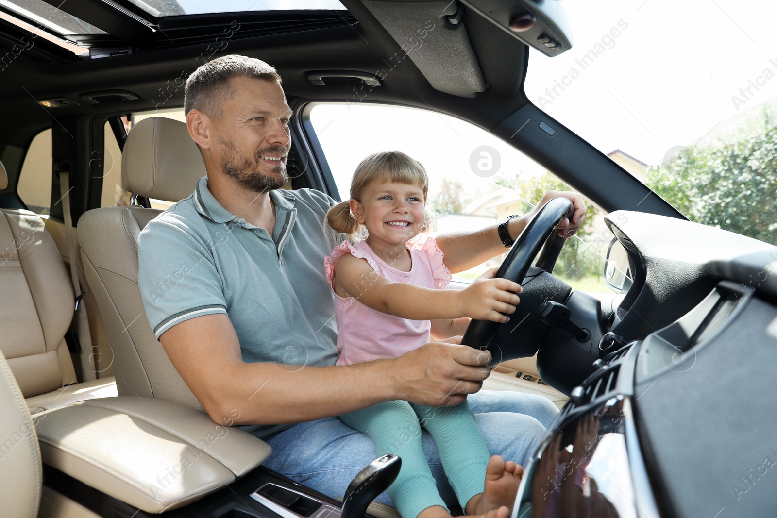 Photo of Happy man with his daughter holding steering wheel inside car