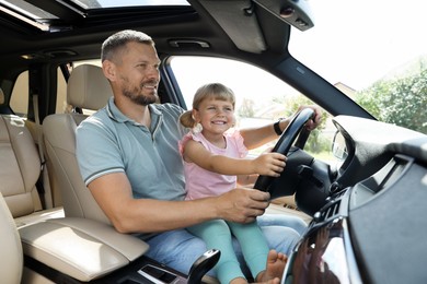 Happy man with his daughter holding steering wheel inside car