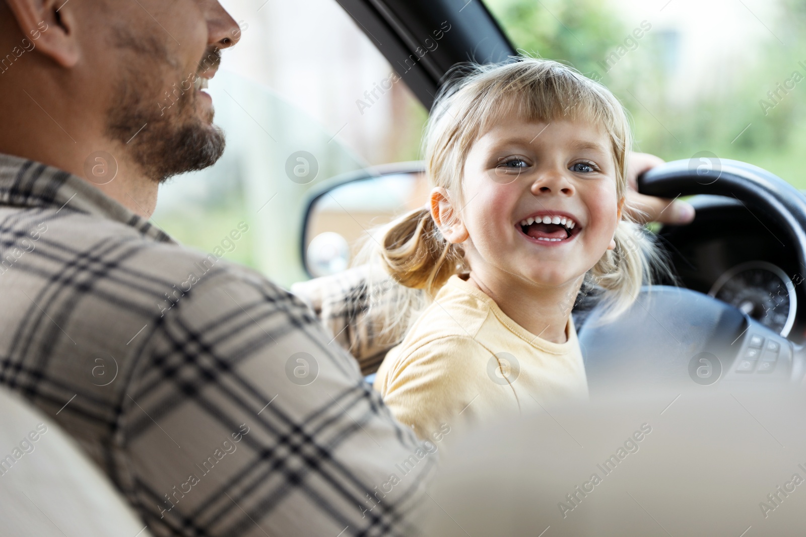 Photo of Man with his daughter holding steering wheel inside car, closeup