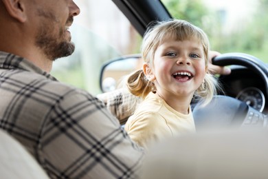 Man with his daughter holding steering wheel inside car, closeup