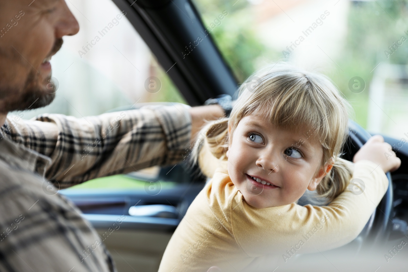 Photo of Man with his daughter holding steering wheel inside car, closeup