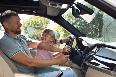 Happy man with his daughter holding steering wheel inside car