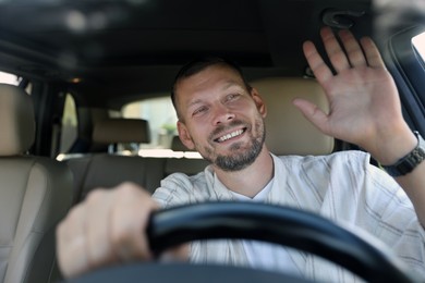 Smiling man holding steering wheel while driving car, view through windshield